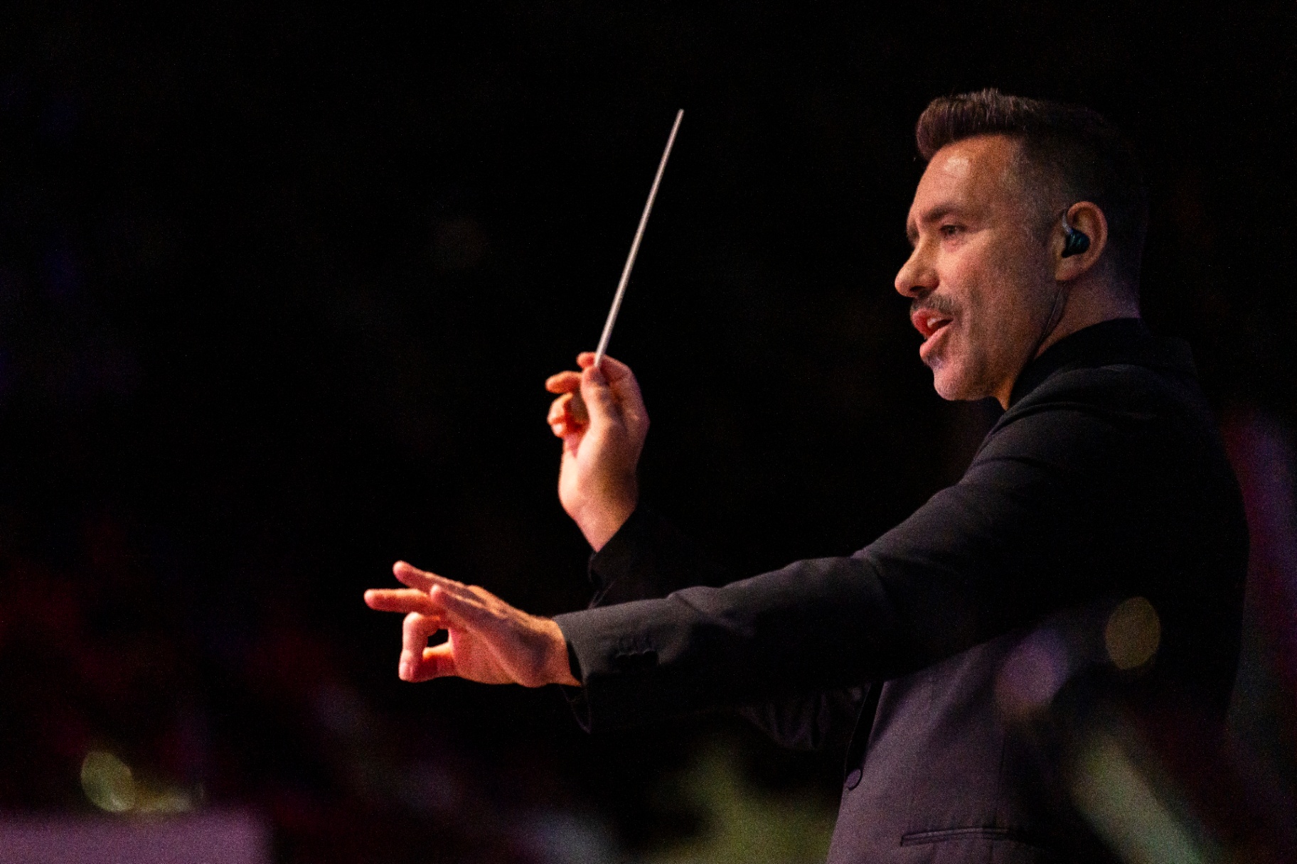 Conductor Jacomo Bairos in profile with baton raised during the Ledisi performance, November 2024