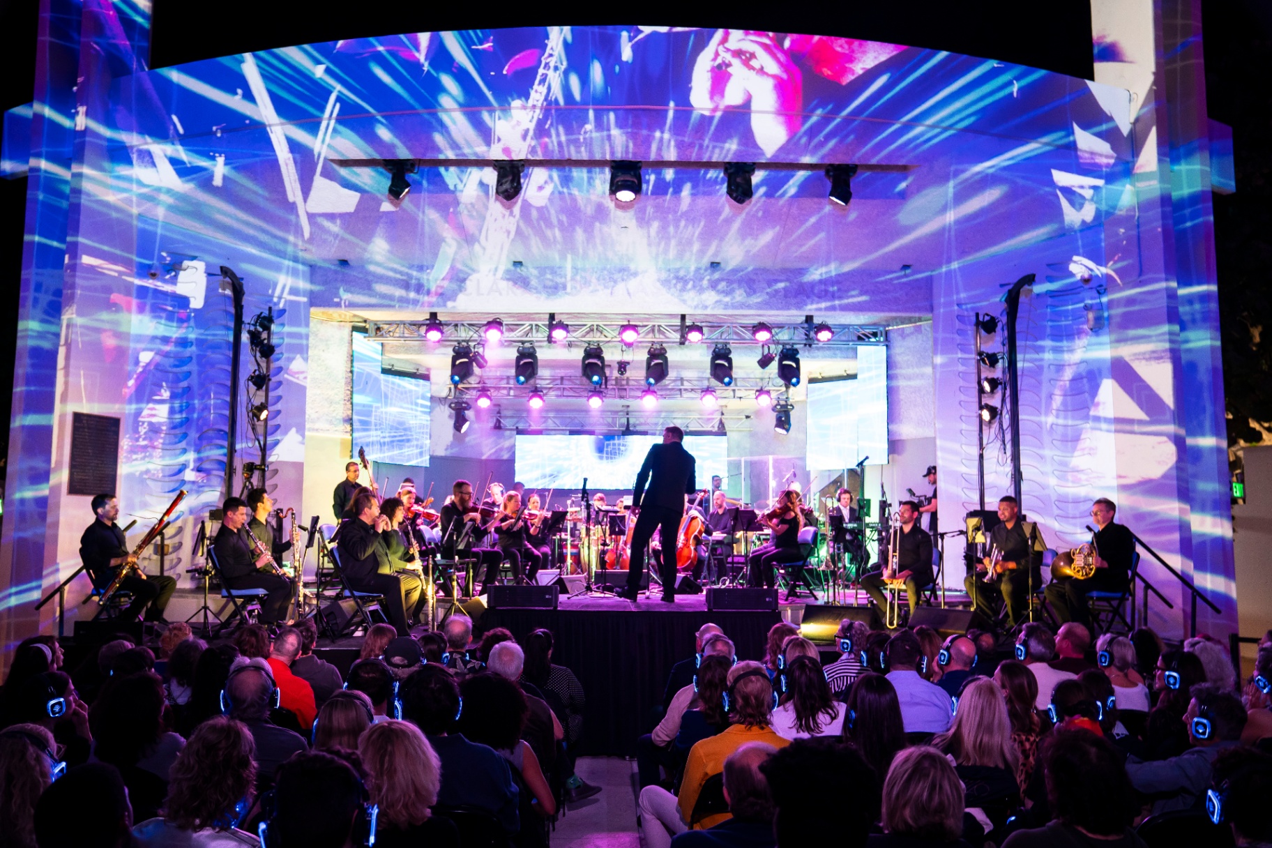 Nu Deco Ensemble conductor leading the orchestra at the Miami Beach Bandshell under blue projections